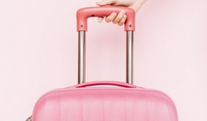 close-up-person-s-hand-holding-handle-travel-baggage-against-pink-background_23-2147958168