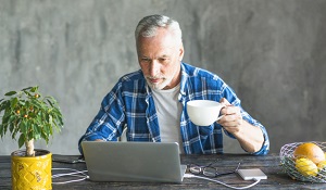 close-up-senior-man-holding-coffee-cup-using-laptop-charged-with-power-bank_23-2147859784